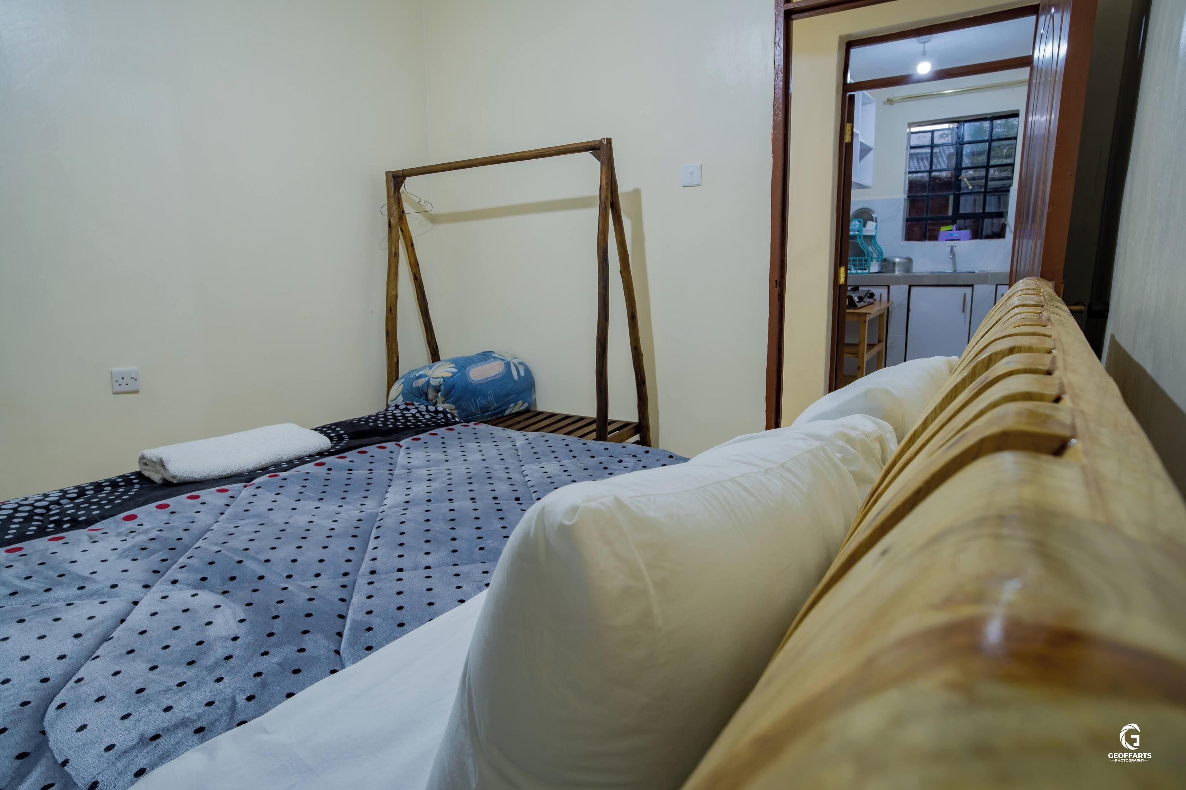 Een slaapkamer met een bed, een houten schommel en uitzicht op een keuken door een deuropening.