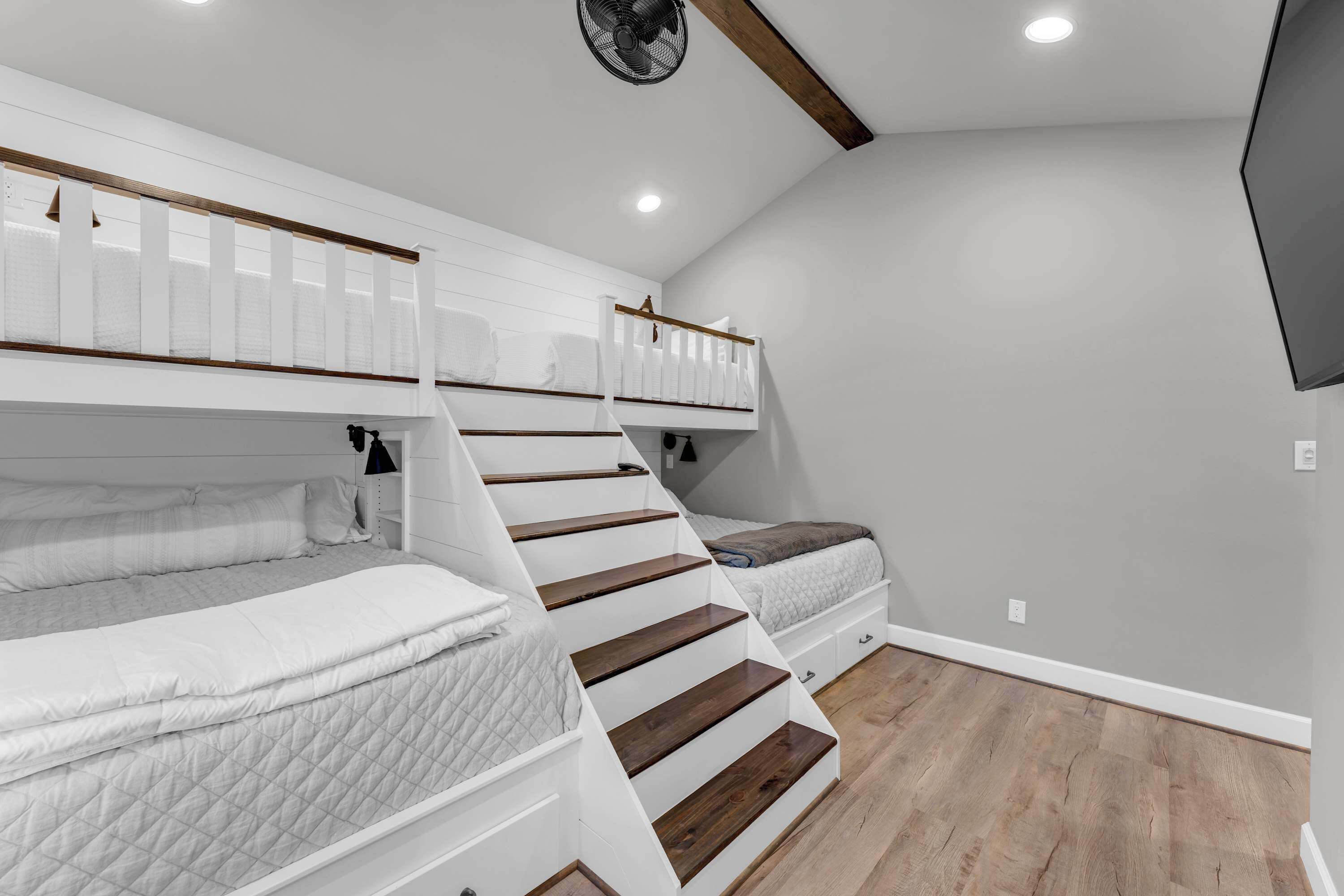 Une chambre avec un lit en mezzanine, un escalier et un téléviseur fixé au mur.