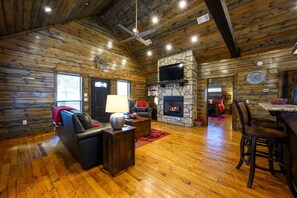 A log cabin interior with a fireplace, leather sofa, and a dining area. - Pond Lily Creek - spacious couples cabin - hot tub (Broken Bow)