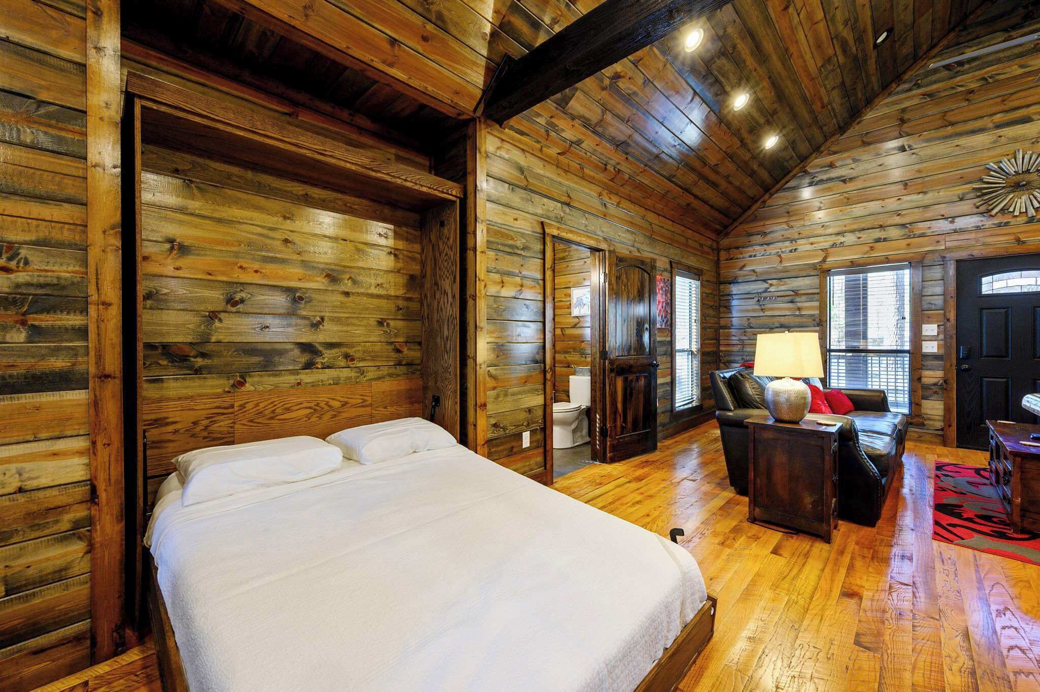 A log cabin-style room with a bed, a sofa, and a small table with a lamp.