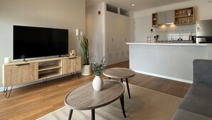 Ein modernes Wohnzimmer mit Fernseher, Holzmöbeln, einem kleinen Tisch mit einer Vase und einem grauen Sofa.