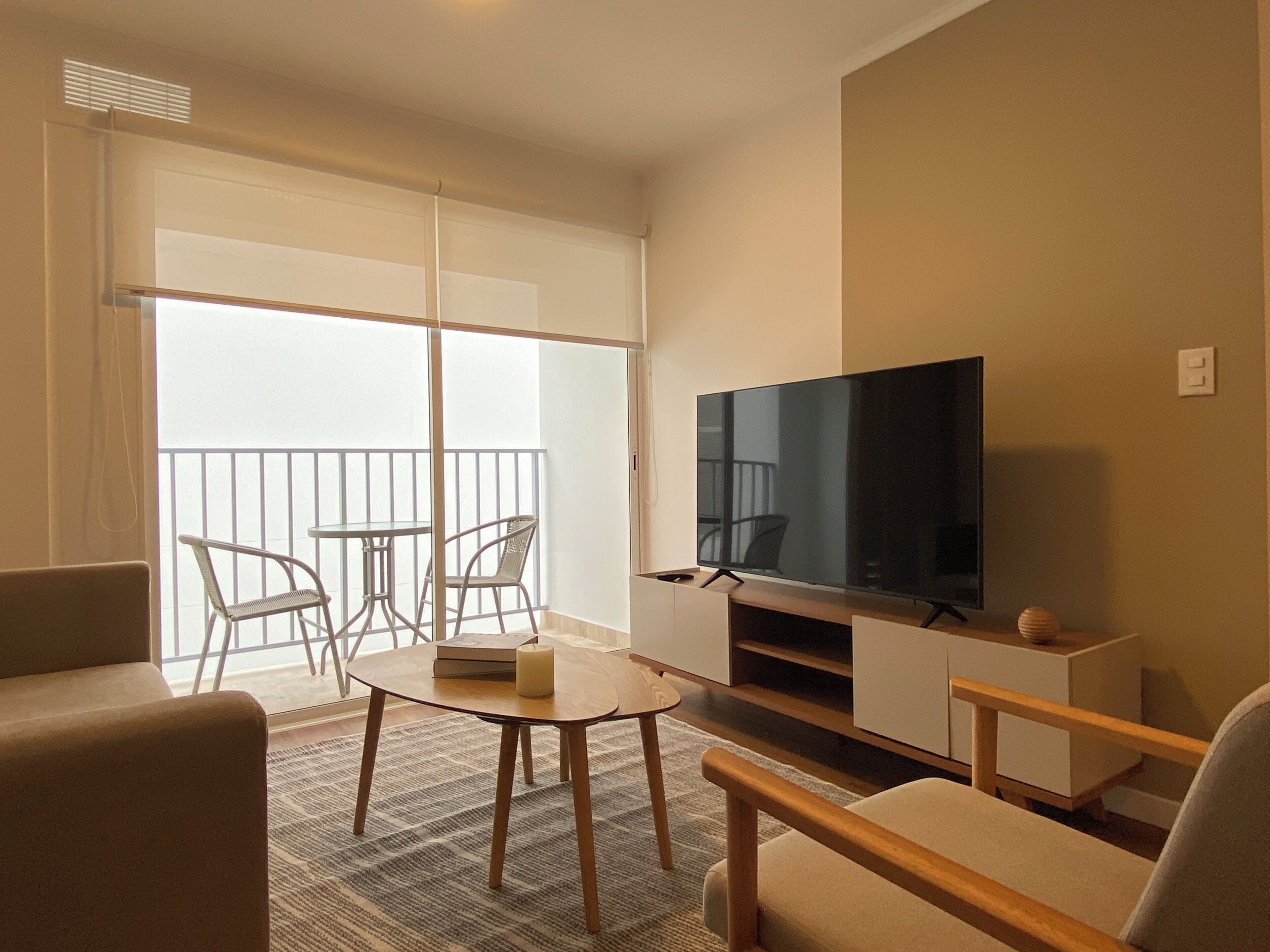 A living room with a TV, a sofa, a chair, a small table, and a balcony with a railing.
