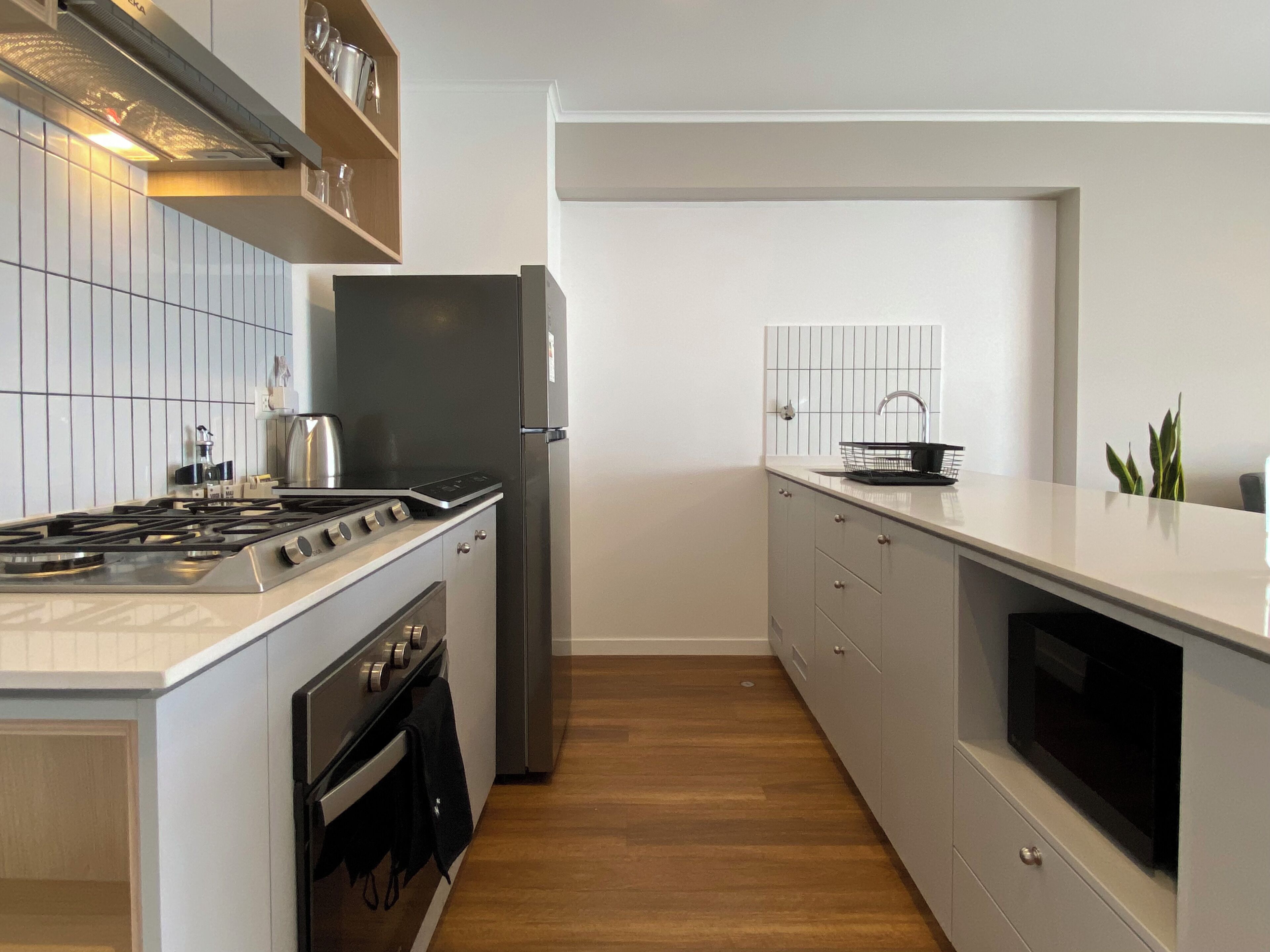 A modern kitchen with a stainless steel stove, refrigerator, and wooden flooring.
