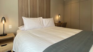 Ein modernes Hotelzimmer mit einem großen Bett, zwei Nachttischen mit Lampen, einem Kleiderschrank und einem hölzernen Kopfteil.