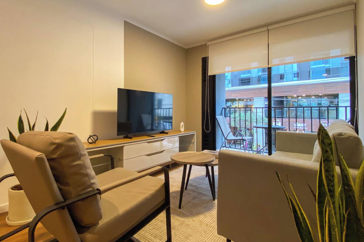 Uma sala de estar moderna com televisão de tela plana, sofá, mesa de centro e varanda com vista para a cidade.