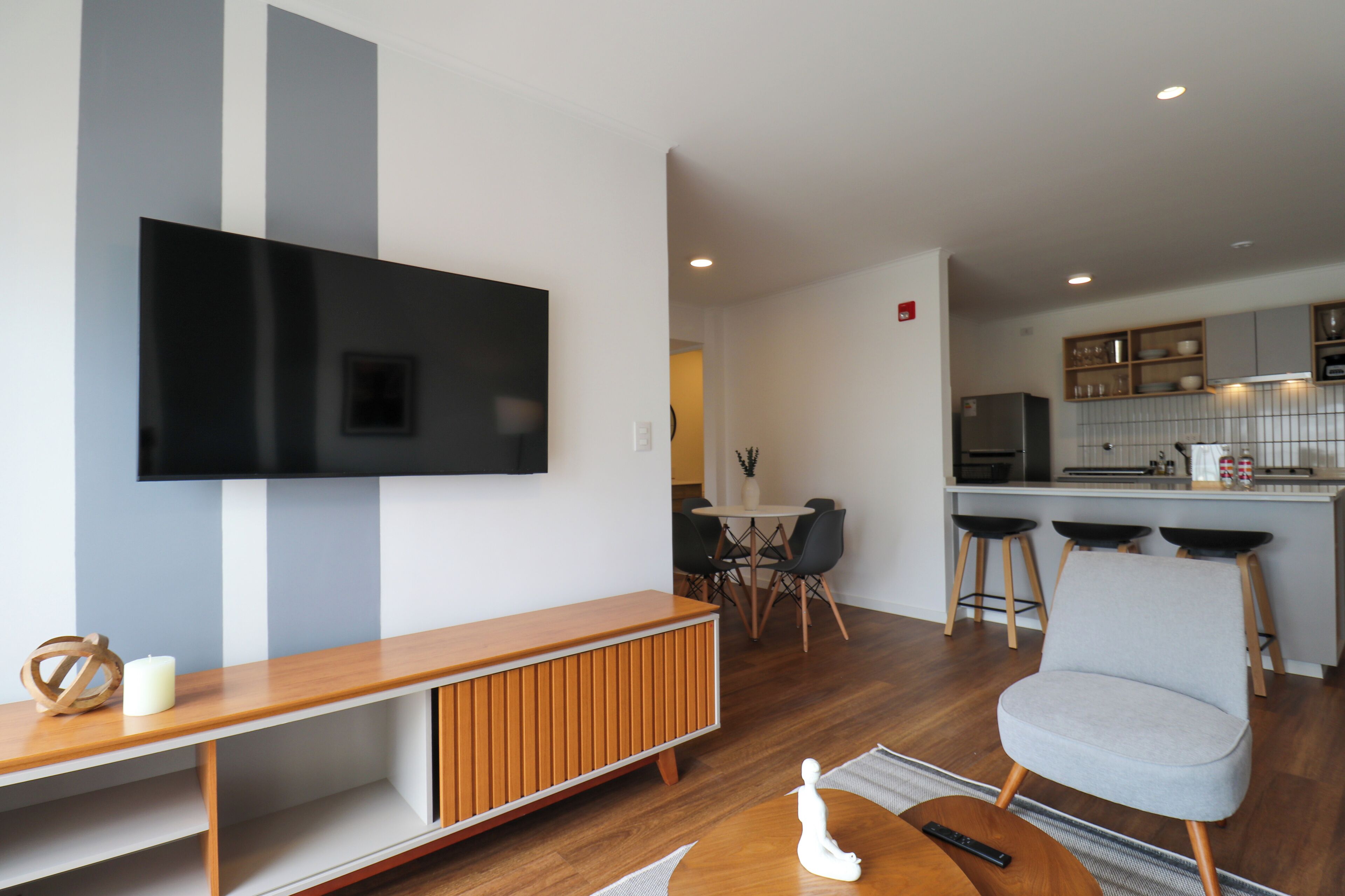 Un soggiorno moderno con una TV a schermo piatto, un mobile TV in legno e una poltrona grigia.