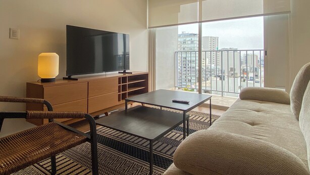 Ein modernes Wohnzimmer mit Flachbildfernseher, einer Couch, einem Couchtisch und einem Balkon mit Blick auf die Stadt.
