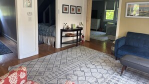 Un saló amb una catifes estampada, un sofà blau, una taula consola fosca amb objectes decoratius, i una escala que mena a una altra habitació.
