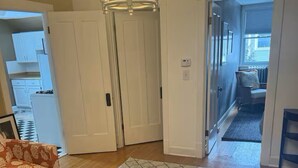 Un saló amb una catifes estampada, un sofà i una cadira. Hi ha una porta que dona a un passadís i una cuina.