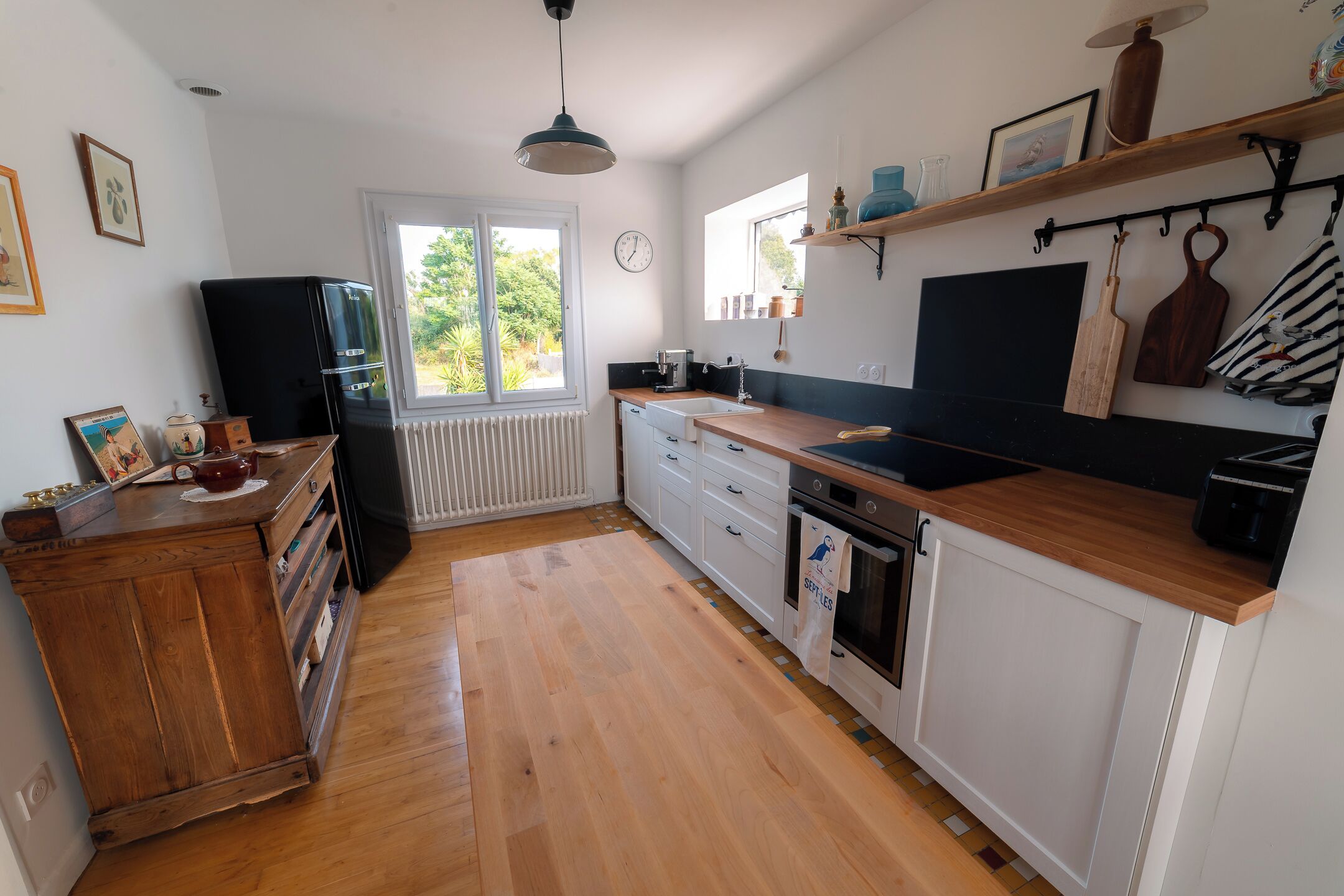Una cucina con mobili in legno, un frigorifero nero, un piano di lavoro in legno e una finestra vista verde.