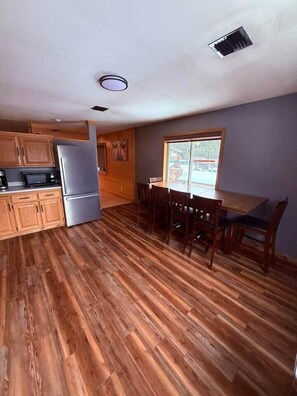 A kitchen with wooden cabinets, a refrigerator, and a dining area with a table and chairs.