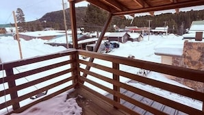Une terrasse en bois dotée d’une rambarde, qui offre une vue sur un paysage enneigé parsemé de bâtiments et d’arbres.