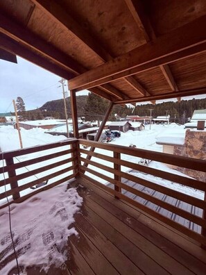 A wooden deck with a railing overlooking a snowy landscape with buildings and trees.