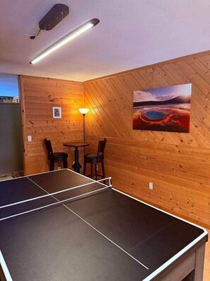 A ping pong table in a room with wooden paneling and a painting of a landscape.