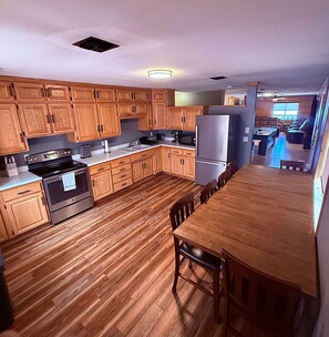 A kitchen with wooden cabinets, a stainless steel refrigerator, and a wooden dining table. - Miller Mountain Cabin (Cooke City)