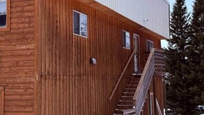 Un bâtiment en bois avec une extension en métal, un escalier et un sol recouvert de neige.