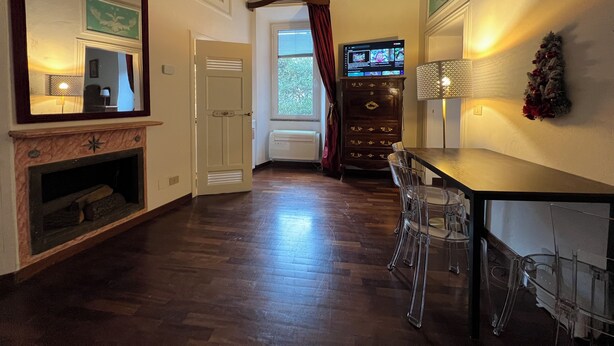 Una stanza con pavimento in legno, un camino, un tavolo da pranzo con sedie, una televisione e un elemento decorativo a parete.