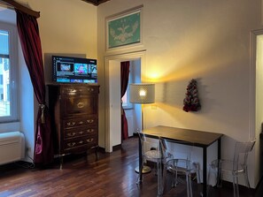 A room with a wooden dresser, a TV on a stand, a small table with chairs, and a Christmas wreath on the wall. - AMAZING TRASTEVERE (Roma)