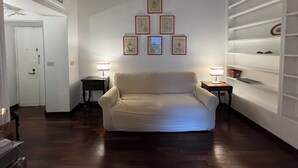 Una stanza con un divano bianco, pavimento in legno, parete bianca con opere d'arte incorniciate e soffitto in legno.