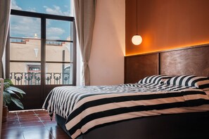 Una camera d'albergo con un letto grande, vista sulla città attraverso una finestra e una testiera in legno.