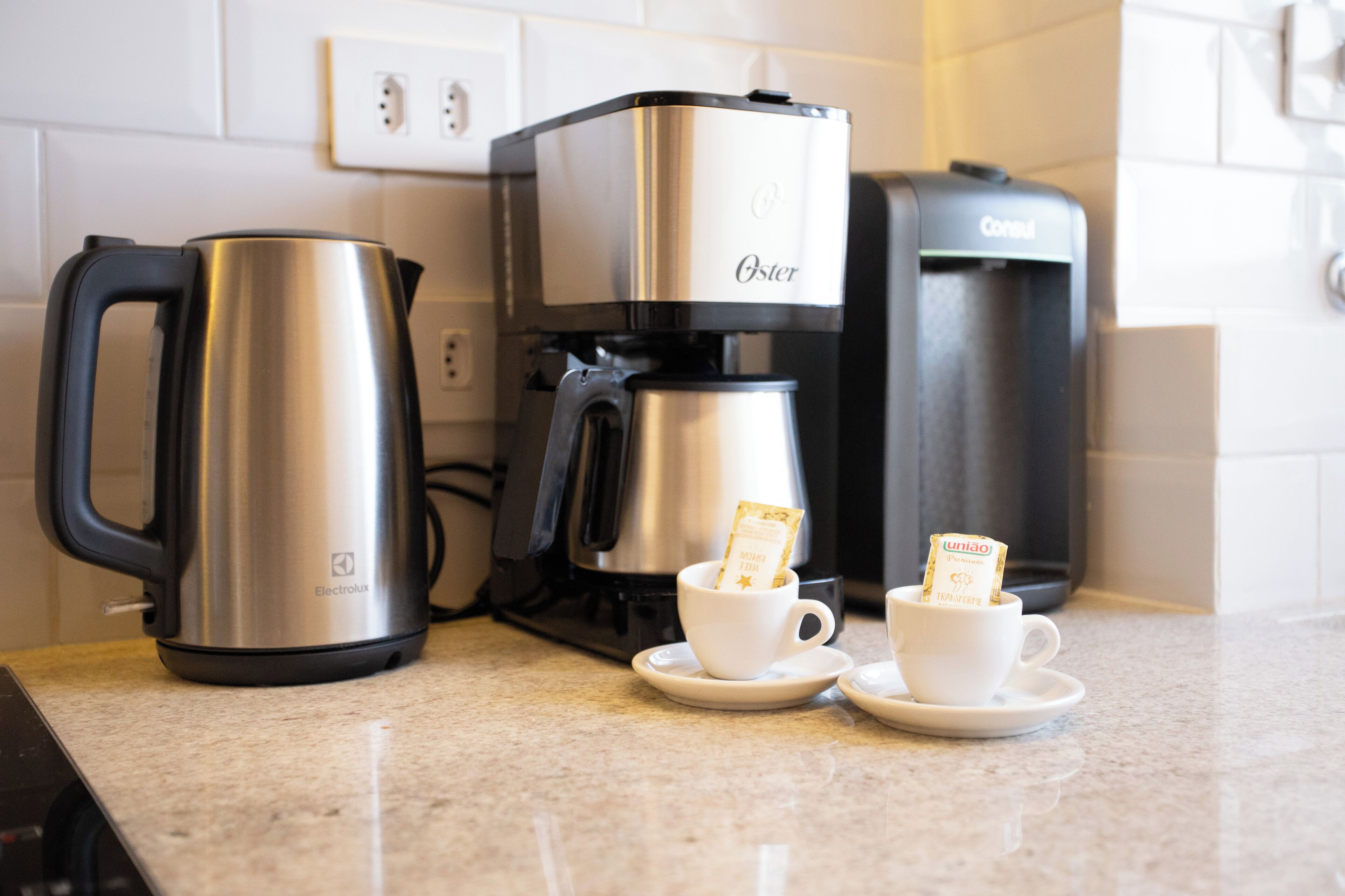 Een koffiezetapparaat, twee kopjes en een waterkoker op een aanrecht.
