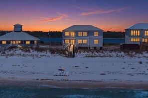 A beachfront property with multiple buildings, a staircase leading to a deck, and a beach area with umbrellas. - Luxury Beachfront House w/pool on Private Beach (Gulf Shores)