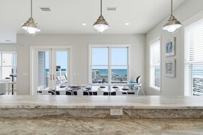 A kitchen with a marble countertop, pendant lights, and a view of the ocean through large windows. - Luxury Beachfront House w/pool on Private Beach (Gulf Shores)