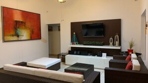 A modern living room with a flat-screen TV, a ceiling fan, a large abstract painting, and a cozy seating area with a sofa and a coffee table. - Cuernavaca In Sumiya San José: dream garden. (Jiutepec)