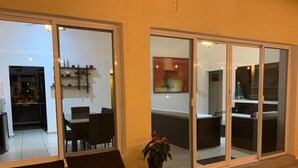 A modern outdoor seating area with a dining table and chairs, a potted plant, and a sliding glass door leading to an interior space with a kitchen and dining area. - Cuernavaca In Sumiya San José: dream garden. (Jiutepec)