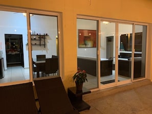A modern outdoor seating area with a dining table and chairs, a potted plant, and a sliding glass door leading to an interior space with a kitchen and dining area. - Cuernavaca In Sumiya San José: dream garden. (Jiutepec)
