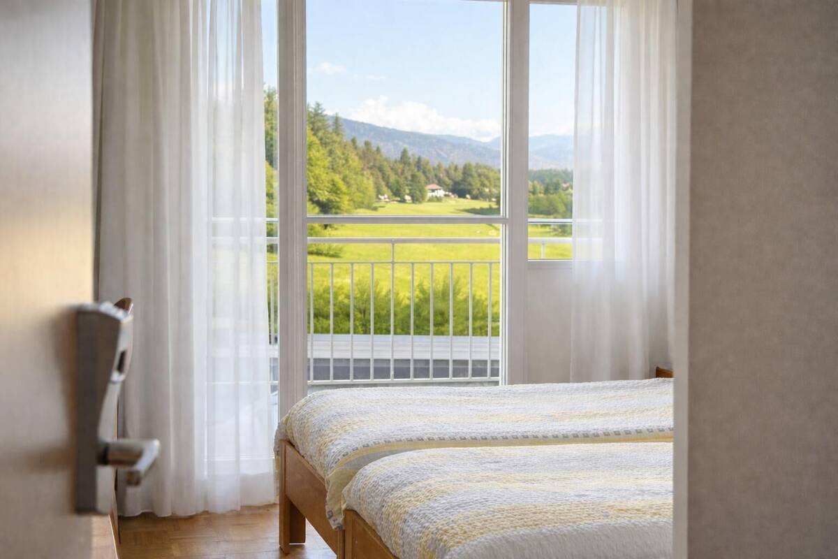 Une chambre avec une grande fenêtre donnant sur un paysage verdoyant et des montagnes.