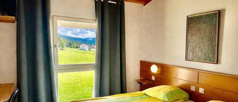 Un dormitorio con cama, mesita de noche, lámpara, ventana con cortinas y un cuadro en la pared.