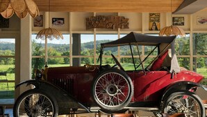 A vintage car displayed indoors with large windows offering a view of a green landscape.