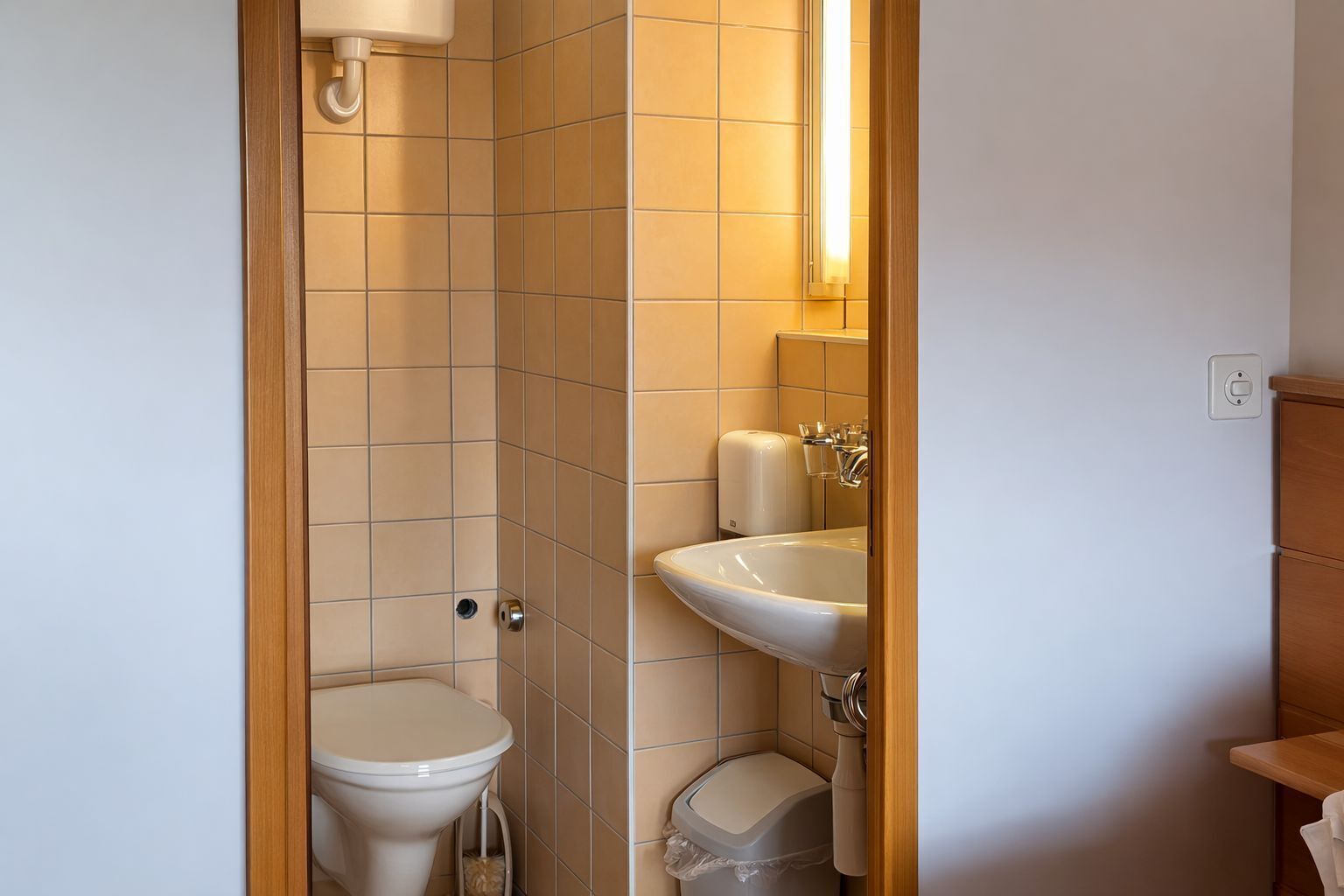 A compact bathroom with a toilet, sink, and a trash bin.