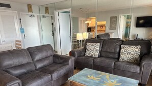 Een woonkamer met twee donker leren banken, een houten salontafel met een bloemmotief, en een keuken op de achtergrond.