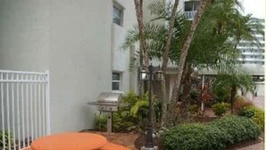 Een terras met een barbecue, een ronde tafel en een witte hek.