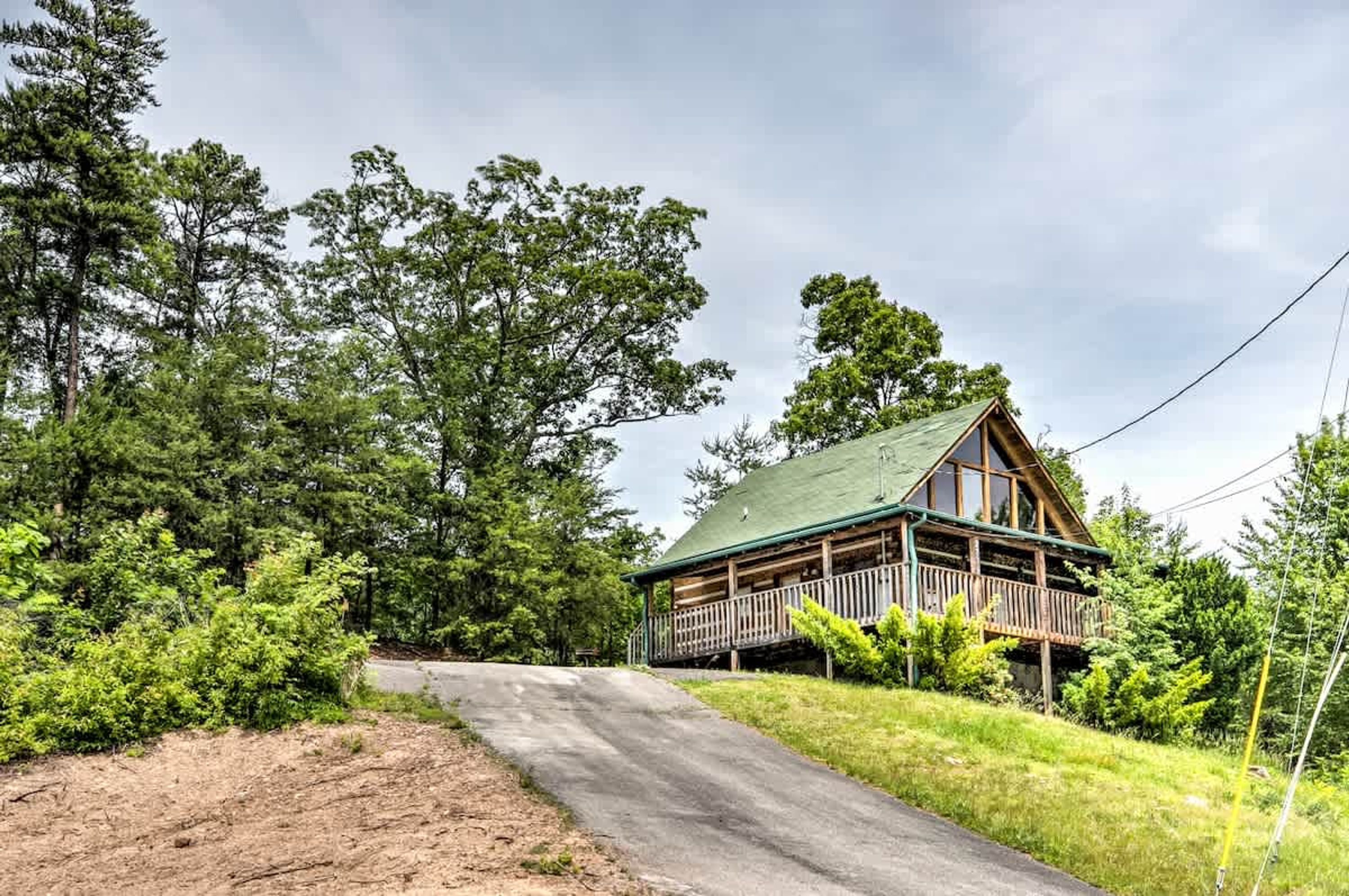 Une cabane en bois dotée d’un porche, entourée d’une forêt dense et bordée d’un chemin de terre.