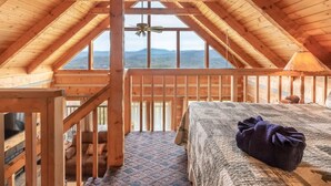 A cozy attic bedroom with a large window, wooden beams, a bed, and a television. - Super View Smoky Mtn Log Cabin Pool Table Hot Tub (Sevierville)