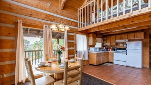 A wooden cabin with a dining area featuring a round table and chairs, a kitchen with wooden cabinets and appliances, and a balcony with a railing. - Super View Smoky Mtn Log Cabin Pool Table Hot Tub (Sevierville)