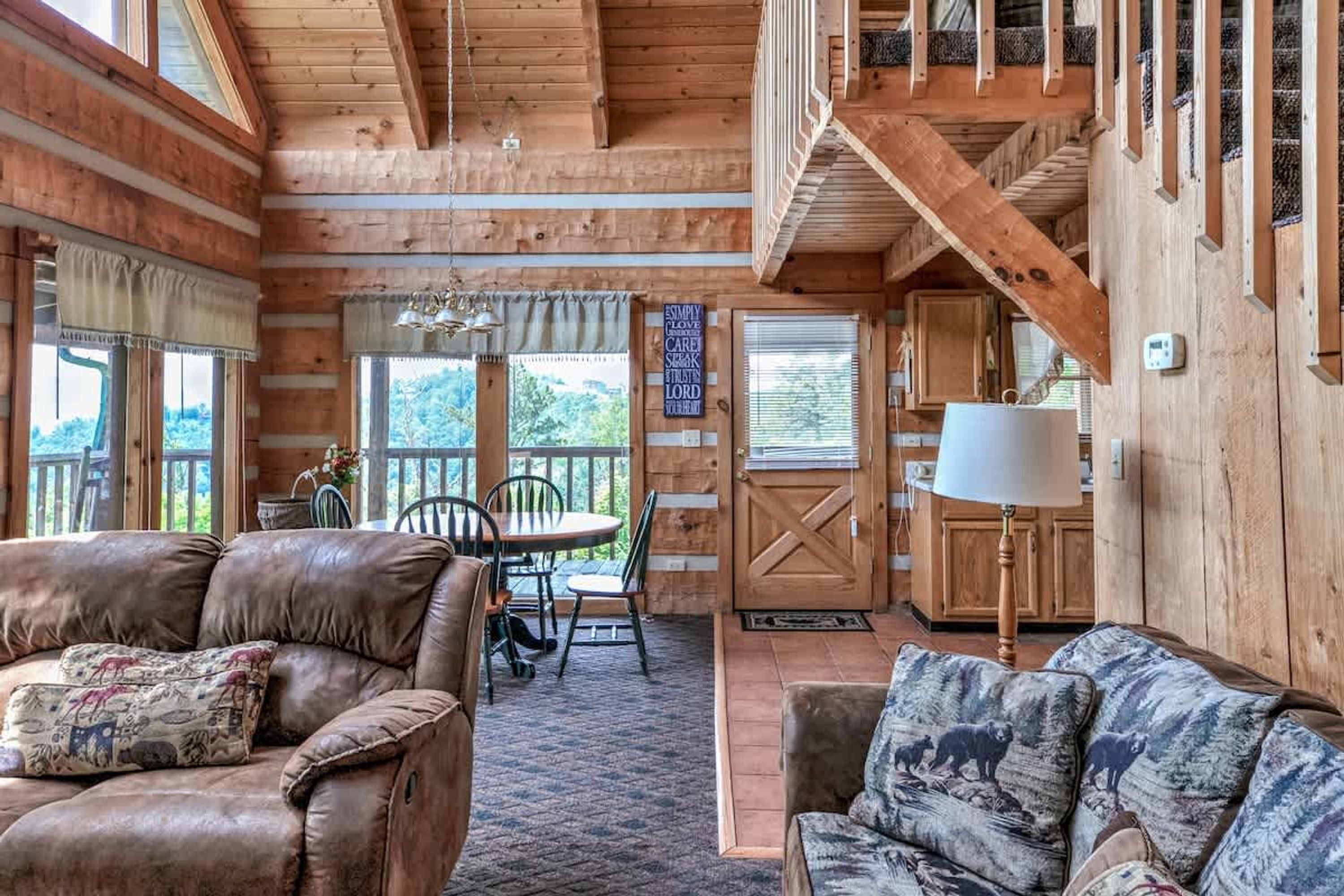 A cozy cabin interior with wooden walls, a dining area, and a staircase.
