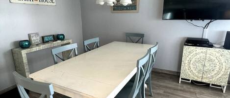 Una zona de menjador amb una taula llarga, sis cadires, un penjoll, un televisor i un armari amb objectes decoratius.