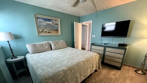 A bedroom with a bed, a dresser, a television, and a painting on the wall. - Beach Pool Open Direct Beachfront Condo Sunsets (Siesta Key)