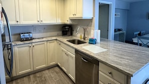 A modern kitchen with white cabinets, a stainless steel sink, and a marble countertop. - Beach Pool Open Direct Beachfront Condo Sunsets (Siesta Key)