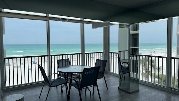 A balcony with a view of the beach, a round table with chairs, and a trash can. - Beach Pool Open Direct Beachfront Condo Sunsets (Siesta Key)