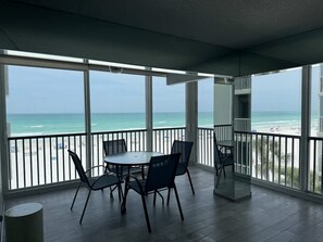 A balcony with a view of the beach, a round table with chairs, and a trash can. - Beach Pool Open Direct Beachfront Condo Sunsets (Siesta Key)