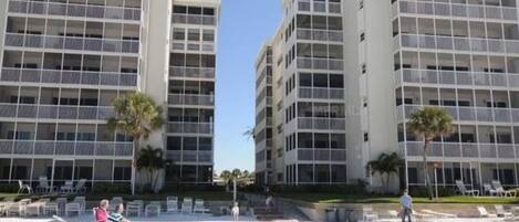 A beachfront hotel with multiple floors, balconies, and a sandy beach area with lounge chairs.