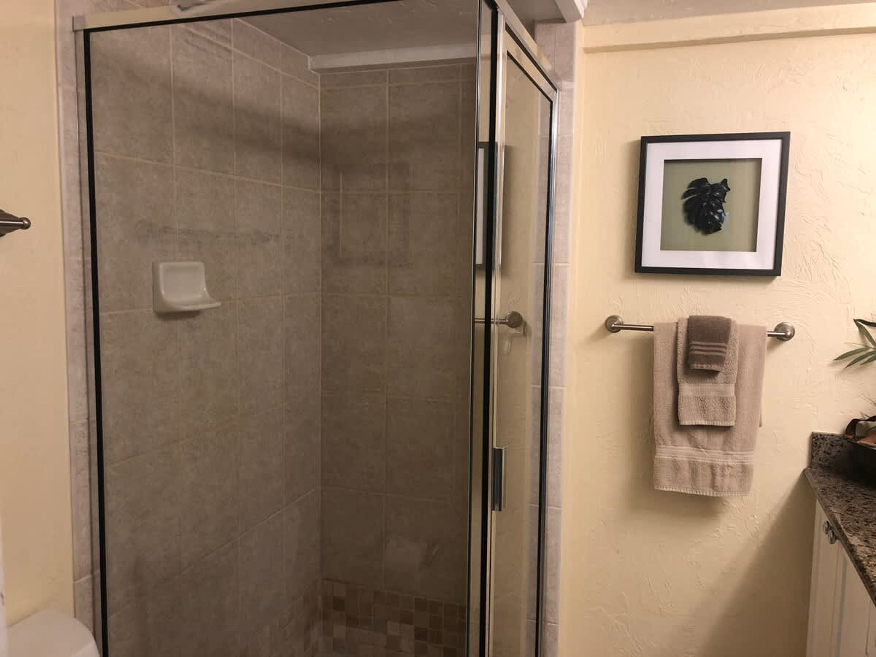 A bathroom with a glass-enclosed shower, a towel rack with towels, and a framed picture on the wall.
