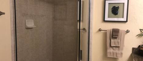 A bathroom with a glass-enclosed shower, a towel rack with towels, and a framed picture on the wall.
