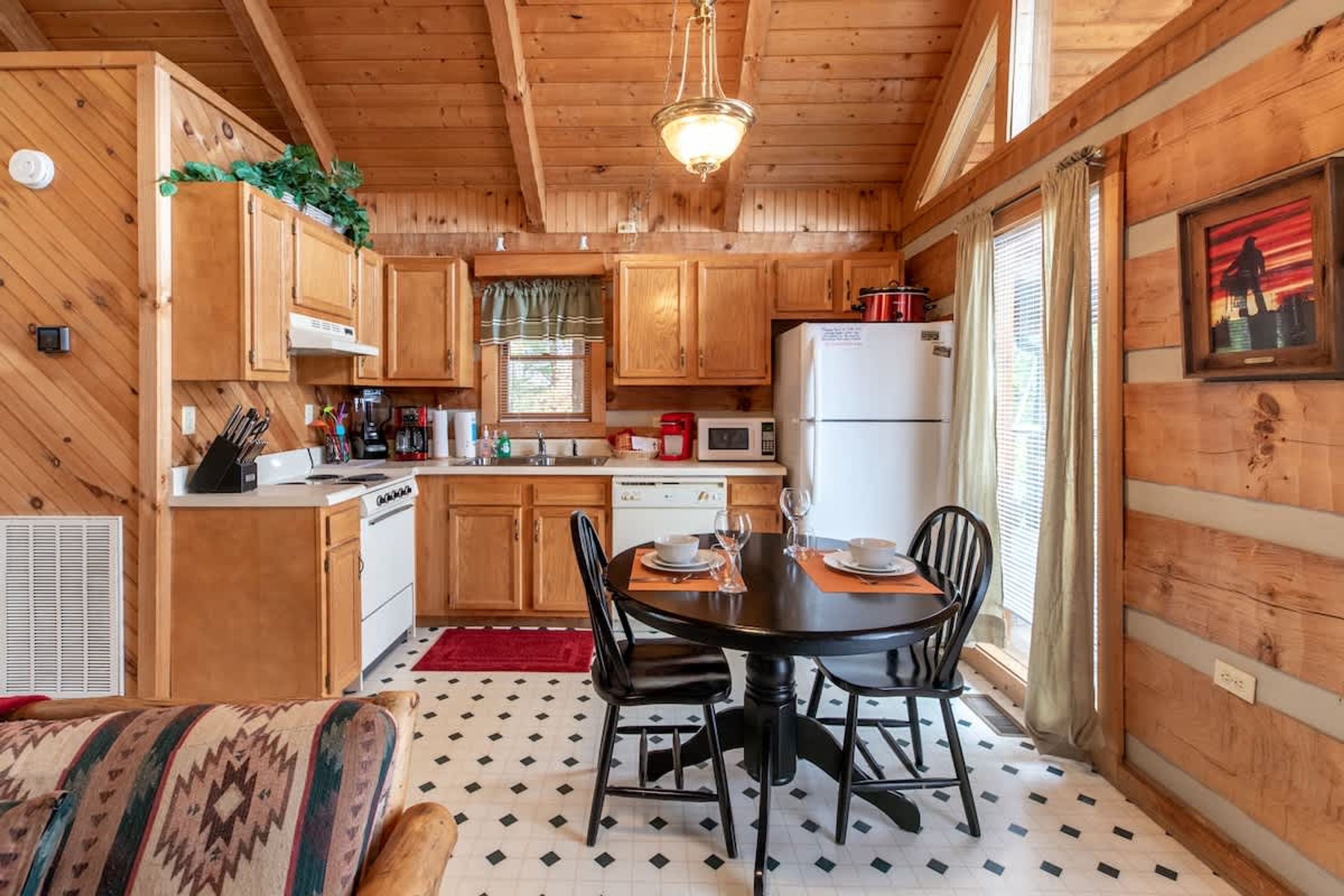 A cozy cabin-style kitchen with wooden cabinets, a dining table with chairs, and a refrigerator.