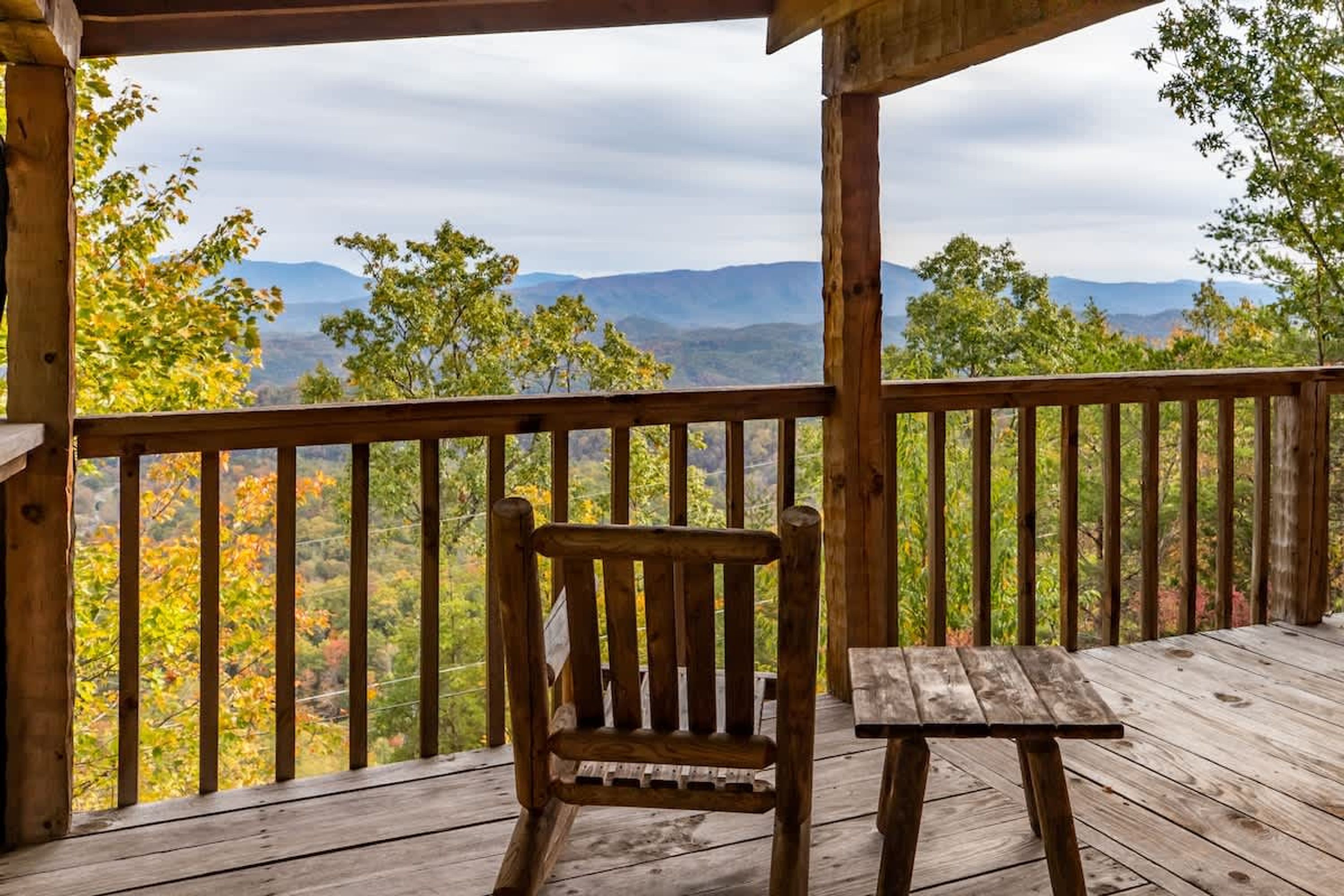 Une terrasse en bois avec une chaise et une table en bois, offrant une vue sur un paysage montagneux aux couleurs automnales.